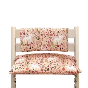 Puede incluir: Una silla alta de madera blanca con un coj&iacute;n y un respaldo con estampado de unicornios rosas y blancos. El coj&iacute;n y el respaldo son extra&iacute;bles.