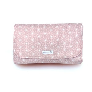 May include: A pink changing mat with a white geometric pattern. The mat has a label that says "Blausberg Baby Hamburg".