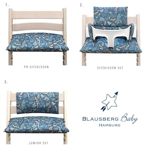 May include: Three different chair cushion sets for a high chair. The cushions are blue with a white and orange pattern of leaves, flowers, and foxes. The sets include a seat cushion, a back cushion, and a tray cushion. The text on the image reads "PO-SITZKISSEN", "SITZKISSEN SET", "JUNIOR SET", "BLAUSBERG Baby HAMBURG".