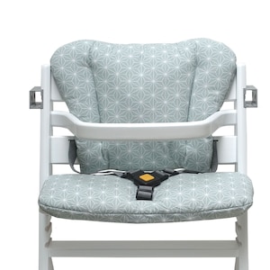 Puede incluir: Silla alta blanca con un cojín de patrón geométrico azul claro y blanco y un arnés de cinco puntos.