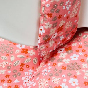 May include: Close-up of a pink fabric with a floral pattern. The fabric has small white, orange, and brown flowers on a pink background.
