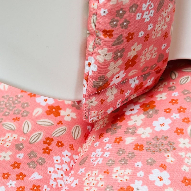 May include: Close-up of a pink fabric with a floral pattern. The fabric has small white, orange, and brown flowers on a pink background.