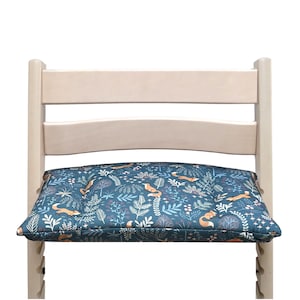 May include: A wooden chair with a blue and orange patterned cushion featuring a woodland design with foxes and leaves. The cushion is padded and provides extra comfort for sitting.