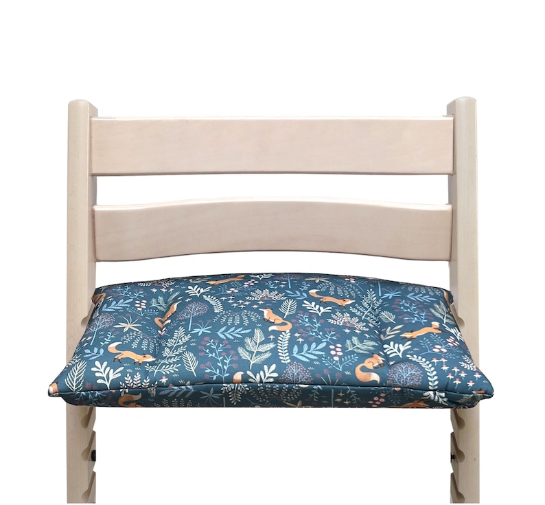 May include: A wooden chair with a blue and orange patterned cushion featuring a woodland design with foxes and leaves. The cushion is padded and provides extra comfort for sitting.