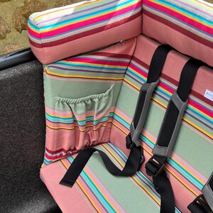 Das rosa-grün-salbei gestreifte Kissen für das Urban Arrow Lastenrad. Das  Lastenrad Kissen für das Urban Arrow wird von der Seite gezeigt. Es verfügt über eine Tasche, in die Kinder während der Fahrt im Lastenrad z.B. eine Trinkflasche stecken können. Es hat eine Nackenrolle, die gut gepolstert und angenehm ist und an die Kinder ihren Kopf sicher lehnen können, wenn sie während der Fahrt im Cargo Bike einschlafen.