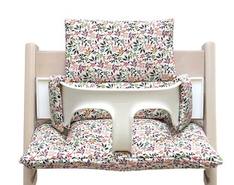 May include: A white high chair with a floral patterned cushion and back support. The cushion has a pink, green, and brown floral pattern.