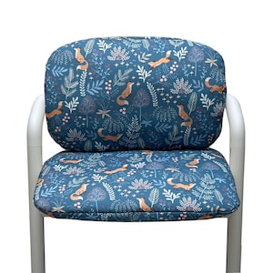 Op de afbeelding: Een stoel met een zitting en rugleuning bedekt met een teal stof. De stof heeft een herhalend patroon van oranje vossen, bomen en bladeren. Het stoelframe is wit.