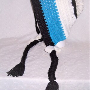 May include: A crocheted hat with a white, blue, and black striped pattern. The hat has a long, black braided tassel on each side.