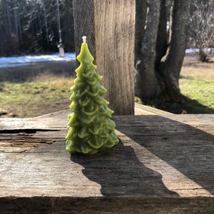 Puede incluir: Una vela verde con forma de árbol de Navidad. La vela está sobre una superficie de madera.