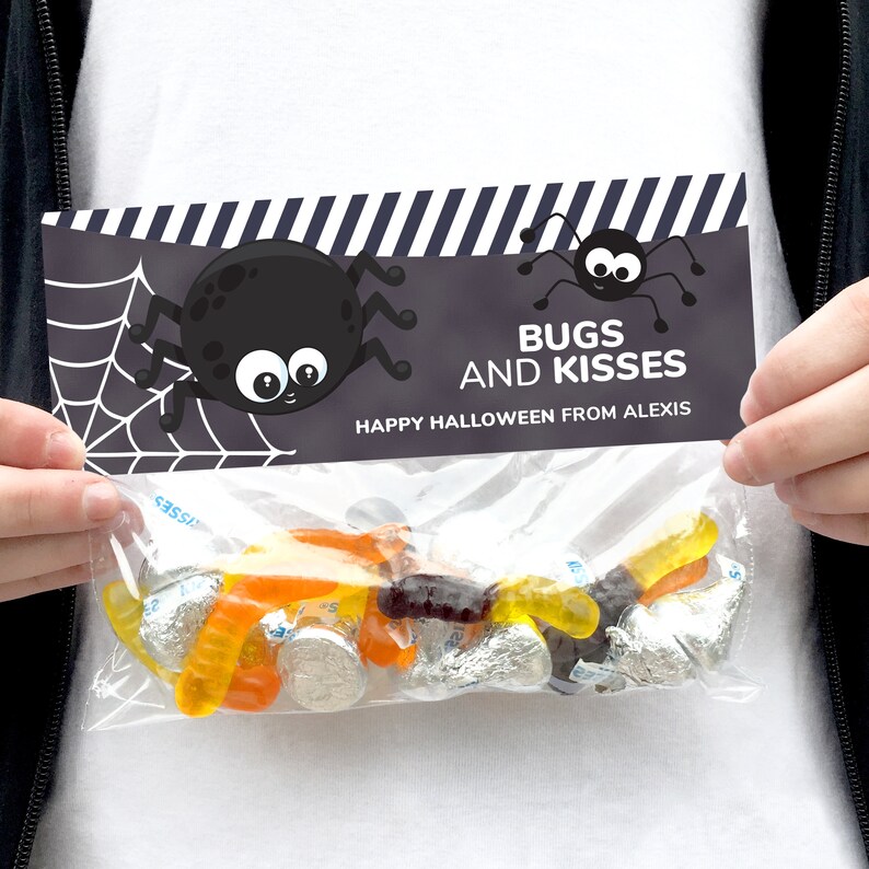 May include: A clear plastic treat bag with a decorative topper featuring a black spider, a white spider web, and the text BUGS AND KISSES HAPPY HALLOWEEN FROM ALEXIS. The bag contains orange and yellow gummy worms and silver foil-wrapped candies.