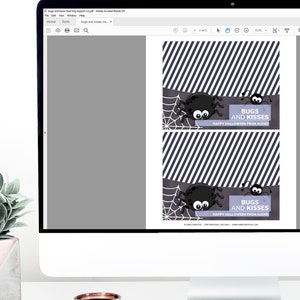May include: A computer monitor displaying a printable PDF file with two identical Halloween treat bag toppers. Each topper features a black and white diagonal striped pattern, a cartoon spider, a spiderweb, and the text BUGS AND KISSES.