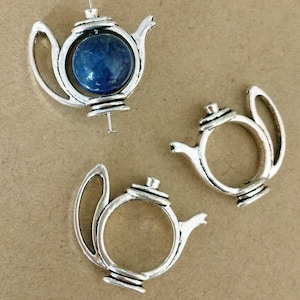 Könnte beinhalten: Drei silberfarbene Teekannen-Anhänger. Einer der Anhänger hat einen blauen Edelstein im Teekannenrahmen. Die Anhänger haben ein Vintage- und Antik-Aussehen. Ideal für Schmuckherstellung oder Bastelprojekte.