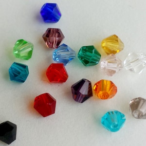 Puede incluir: Una colección de cuentas facetadas de varios colores, incluyendo azul, verde, rojo y amarillo. Las cuentas tienen forma hexagonal y parecen estar hechas de vidrio o cristal, adecuadas para la fabricación de joyas o proyectos de artesanía.