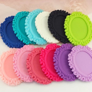 Puede incluir: Una colección de marcos decorativos ovalados en varios colores, incluyendo azul, turquesa, blanco, negro, verde, rosa, rojo y morado. Cada marco presenta un diseño de borde ornamental y enrollado, ideal para manualidades.