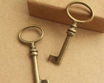 May include: Two antique-style keys with an aged brass finish. The keys have an oval loop at the top and a detailed stem. One key is positioned diagonally, and the other is upright. The background is a light brown.