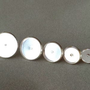 May include: A collection of five silver-toned, round bezel settings in varying sizes. Each setting features a flat, reflective surface within a raised, circular frame. The bezels are arranged in a diagonal line, showcasing their graduated sizes.