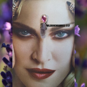 May include: A pink crystal with a gold setting and a pink gem on top. The crystal is worn as a forehead adornment. WILDBOHEMIANROSE ETSY is written on the image.