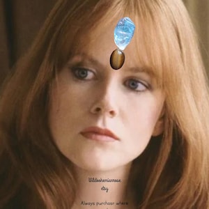 May include: A light blue translucent crystal and a brown oval tiger's eye stone positioned on the forehead. The text Wildbohemianrose etsy Always purchasr where you see my logo name is printed in black on the lower portion of the image.