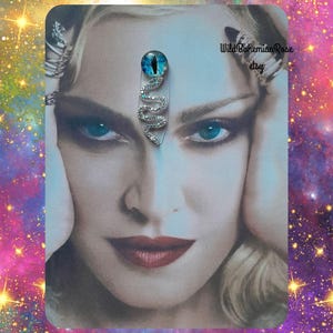 May include: A portrait with a decorative snake pin. The pin features a blue eye and a silver, rhinestone-studded snake design. The background is a colorful galaxy design with the text "Wild Bohemian Rose etsy".