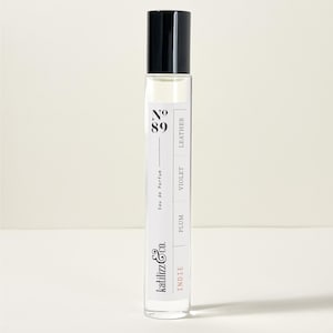 May include: A clear glass roll-on bottle of perfume labeled "Indie" with the brand name "katilizza & co." and the number "89". The bottle has a black cap and the label lists the notes "Plum", "Violet", and "Leather".
