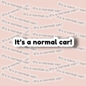 May include: A white sticker with the text "It's a normal car!" in black, surrounded by a black border. The sticker is on a light pink background with blurred text that reads "It's a normal car!" repeated.