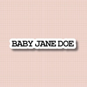 Könnte beinhalten: Ein weißer Aufkleber mit dem Text "BABY JANE DOE" in fetter, schwarzer Schrift. Der Aufkleber ist rechteckig mit abgerundeten Ecken und einem weißen Rand. Der Hintergrund ist ein hellrosa Gittermuster.