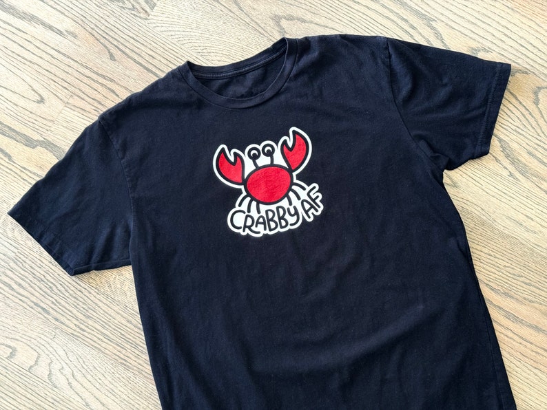 blackt-shirt with a minimalist graphic crab illustration with hand lettering Crabby AF