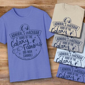 A light blue, sand, sport grey, and heather royal Star Wars t-shirt with a navy blue graphic print of a logo for a snack bar called 'Admiral's Snack Bar.' The logo features Admiral Ackbar, with the text 'Home of the Galaxy Famous Obi-Wan Cannoli.' The text 'Served 'Vader-style' (sliced in half)' is printed below the logo.