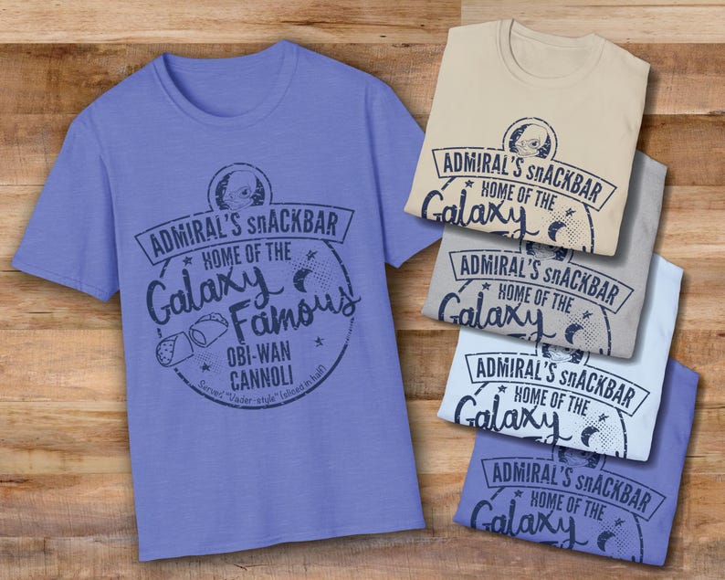 A light blue, sand, sport grey, and heather royal Star Wars t-shirt with a navy blue graphic print of a logo for a snack bar called 'Admiral's Snack Bar.' The logo features Admiral Ackbar, with the text 'Home of the Galaxy Famous Obi-Wan Cannoli.' The text 'Served 'Vader-style' (sliced in half)' is printed below the logo.