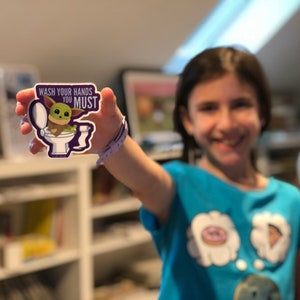 Vibrant Baby Yoda vinyl sticker. Baby Yoda is sitting on the toilet saying Wash Your Hands You Must