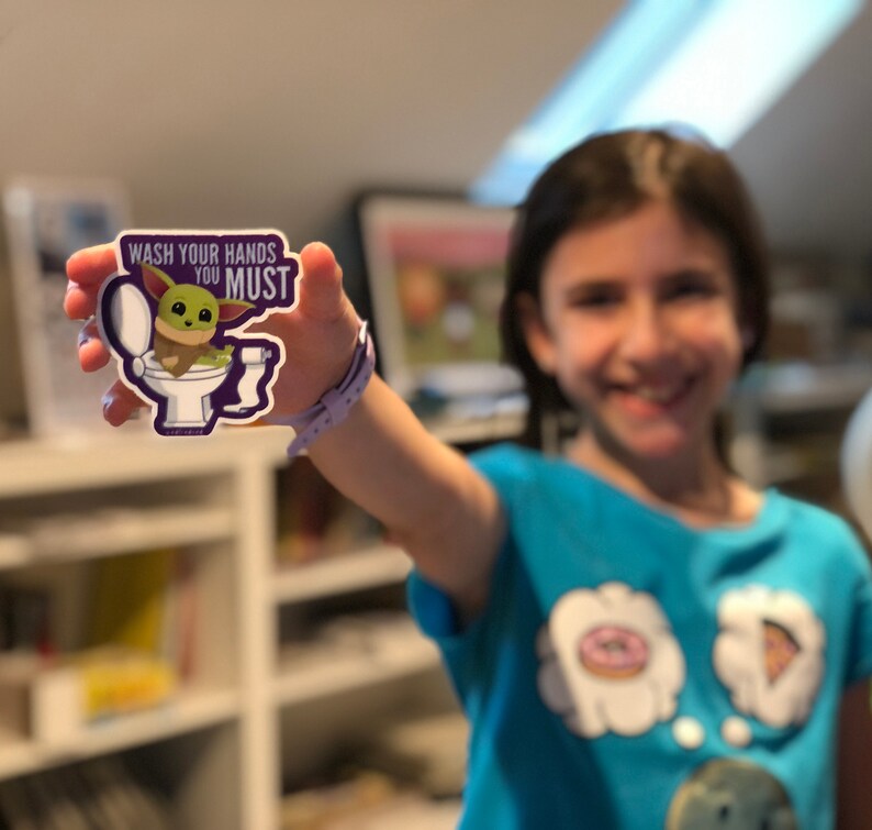 Vibrant Baby Yoda vinyl sticker. Baby Yoda is sitting on the toilet saying Wash Your Hands You Must