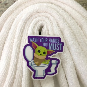 Vibrant Baby Yoda vinyl sticker. Baby Yoda is sitting on the toilet saying Wash Your Hands You Must