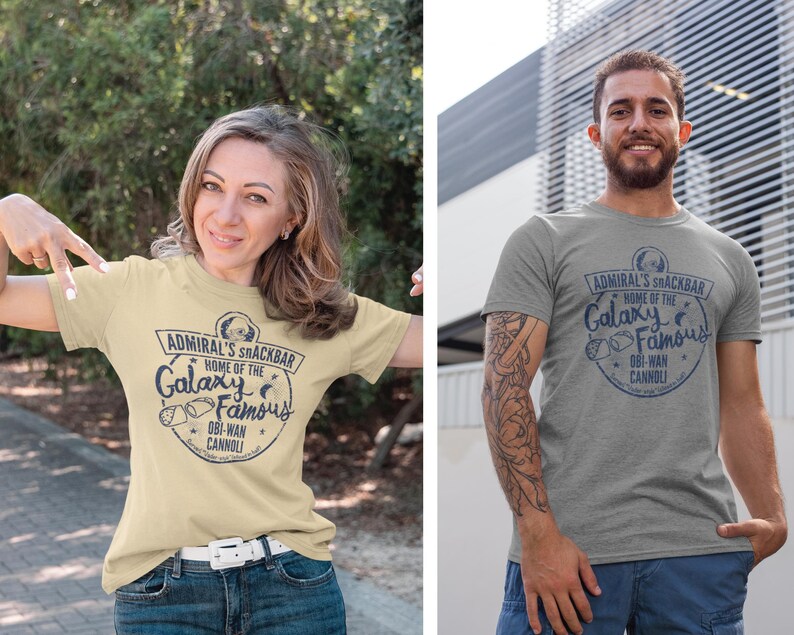 A woman and man wearing a Star Wars t-shirt with a navy blue graphic print of a logo for a snack bar called 'Admiral's Snack Bar.' The logo features Admiral Ackbar, with the text 'Home of the Galaxy Famous Obi-Wan Cannoli.' The text 'Served 'Vader-style' (sliced in half)' is printed below the logo.