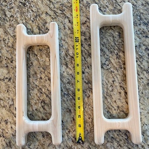 以下が含まれることがあります： 2つの木製フレーム、1つは高さ28cm、もう1つは高さ43cmです。両方のフレームは未仕上げの明るい木材でできており、丸みを帯びた角を持つシンプルな長方形の形をしています。