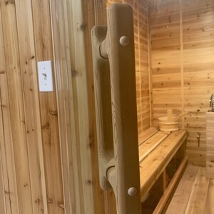 以下が含まれることがあります： 丸みを帯びた長方形の形状で、滑らかな明るい茶色の仕上げが施された木製ドアハンドル。ハンドルには両側に白いノブが2つあります。