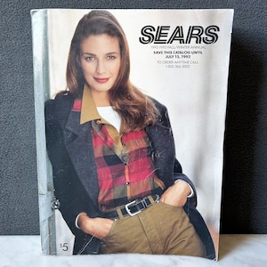 Könnte beinhalten: Ein Vintage-Sears-Katalogcover mit einer Frau in einem karierten Hemd, einer khakifarbenen Hose und einem dunklen Blazer. Das Katalogcover trägt den Text "SEARS" und "1992-1993 FALL/WINTER ANNUAL". Das Katalogcover ist mit einem Preis von 5 $ versehen.