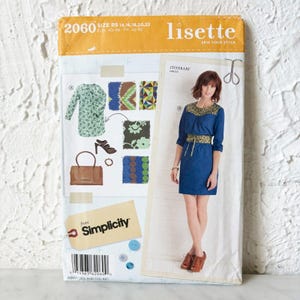 May include: A Lisette 2060 sewing pattern envelope for an Itinerary dress. The package features a blue dress with a patterned yoke and waist, a green patterned dress, a brown handbag, and shoes. The Simplicity logo is printed on the front.