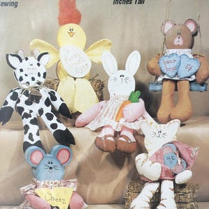 May include: Six hand-painted fabric animal figurines, each approximately 6 to 11 inches tall. The figurines include a giraffe, a chick, a bunny, a bear, a cat, and a mouse. The figurines are painted in various colors, including black, white, yellow, pink, brown, and blue. The figurines are all sitting on a straw-like surface.