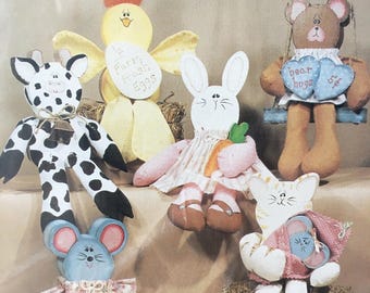 Puede incluir: Seis figuritas de animales de tela pintadas a mano, cada una de aproximadamente 15 a 28 cm de alto. Las figuritas incluyen una jirafa, un pollito, un conejito, un oso, un gato y un ratón. Las figuritas están pintadas en varios colores, incluyendo negro, blanco, amarillo, rosa, marrón y azul. Las figuritas están todas sentadas sobre una superficie de paja.