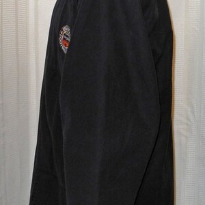 May include: A black long-sleeved jacket with a zipper closure and a circular patch on the left sleeve that says "Batman" with a bat logo.