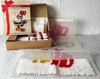 May include: A vintage Christmas Ho Ho Santa latch hook kit. The kit includes a cardboard box, a printed pattern, yarn, and a hook. The finished design features Santa Claus with the words "Ho Ho". The finished size is 17" x 30".