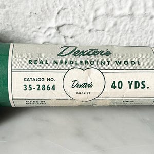 May include: A skein of dark green wool yarn labeled "Dexter's Real Needlepoint Wool" with a catalog number of 35-2864 and a length of 40 yards.