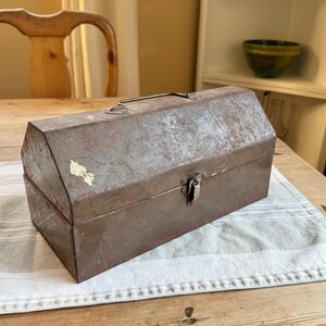 May include: A vintage metal toolbox with a hinged lid and a latch. The toolbox is rusty and has a worn, faded paint finish.