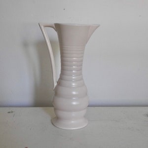 May include: A white ceramic pitcher with a fluted design and a curved handle. The pitcher has a rounded base and a wide mouth.