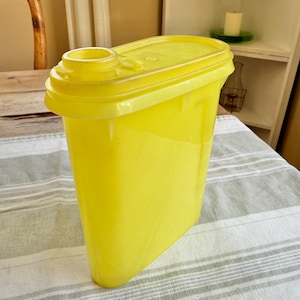 May include: A bright yellow plastic container with a lid and a spout. The container is designed for storing dry goods like cereal or sugar.