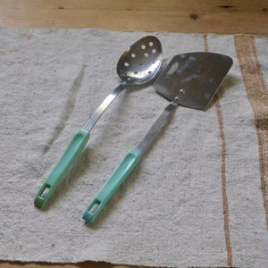 May include: Two kitchen utensils with light green handles. A slotted spoon and a spatula.