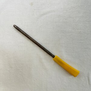 May include: A yellow handled metal knife sharpener on a white tablecloth with a floral border.