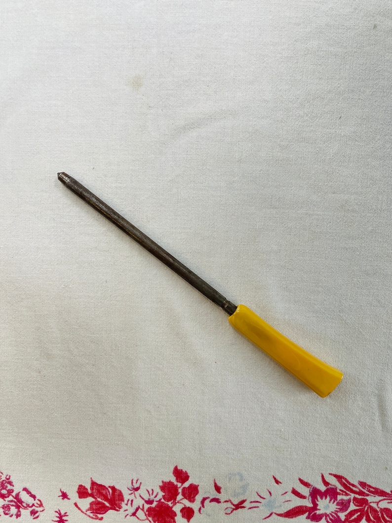 May include: A yellow handled metal knife sharpener on a white tablecloth with a floral border.