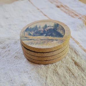 May include: A set of four brown cork coasters with a printed image of two bears cuddling in a forest setting.