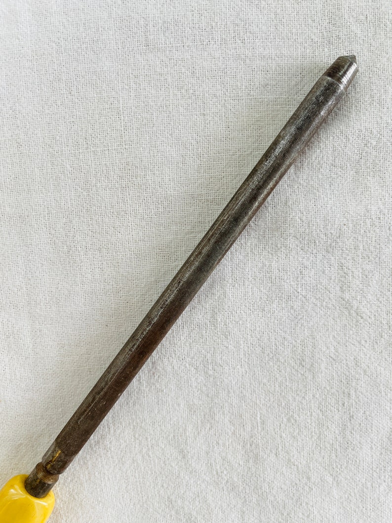 May include: A close-up of a metal sharpening steel with a yellow plastic handle. The steel is used to sharpen knives.